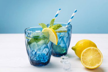 Limon ve limonlarla süslenmiş beyaz ahşap masa üzerinde limonlu buzlu su bardakları. Taze narenciye suyu, ferahlatıcı içecek, limonata..