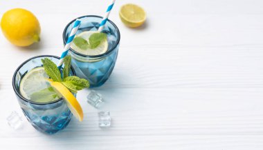 Limon ve limonla süslenmiş beyaz ahşap masa üzerinde bir bardak limonlu buzlu su. Taze narenciye suyu. Ev yapımı ferahlatıcı içecek boş fotokopi alanı..