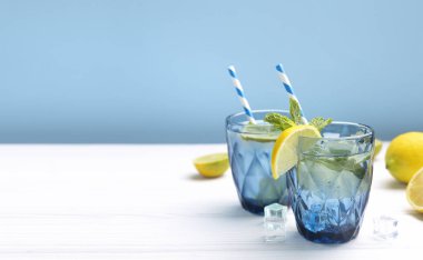 Limon ve limonla süslenmiş beyaz ahşap masa üzerinde bir bardak limonlu buzlu su. Taze narenciye suyu. Ev yapımı ferahlatıcı içecek boş fotokopi alanı..