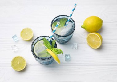 Limon ve limonla süslenmiş beyaz ahşap masa üzerinde bir bardak limonlu buzlu su. Taze narenciye suyu. Ev yapımı ferahlatıcı içecek. Daha hafif bir içecek. Limonata..