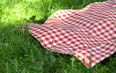 Kırmızı kareli piknik havlusu çimenlerin üzerinde ekose kumaş, açık havada masa örtüsü. Yemek reklamı yaz şablonu..