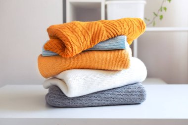 Masaya bir yığın katlanmış kıyafet. Örgü yığını. Yünlü kazaklar. İtiraz yok..