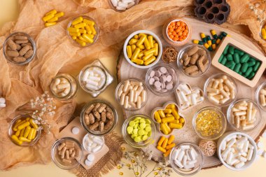 Big amount of various dietary supplements pills, vitamins, minerals, tablets and capsules in small jars from above on a wooden desk on beige background in rustic style. Healthy lifestyle. clipart