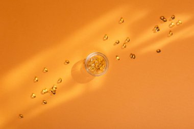 D vitamini kapsülleri turuncu arka plan manzaralı güneş ışığı altında. Vitamin D3 kapsülleri ve güneş ışığı. 