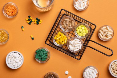 Renkli haplar ve diyet takviyeleri yukarıdan turuncu arka planda küçük cam kaselerde. Vitamin ve mineral grupları üst görüntüde. Kırsal tarzda. Sağlıklı yaşam tarzı