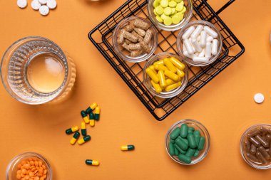 Küçük cam kaselerde renkli haplar ve diyet takviyeleri ve turuncu arka planda yukarıdan bir bardak su. Vitamin ve mineral grupları üst görüntüde. Kırsal tarzda. Sağlıklı yaşam tarzı.