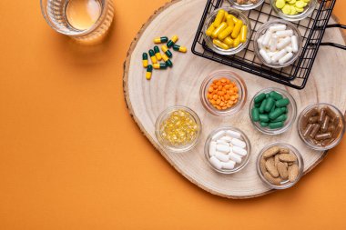 Küçük cam kaselerde renkli haplar ve diyet takviyeleri ve turuncu arka planda yukarıdan bir bardak su. Vitamin ve mineral grupları üst görüntüde. Kırsal tarzda. Sağlıklı yaşam tarzı.