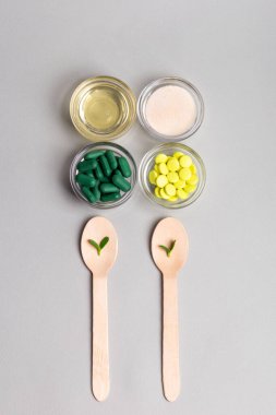 Homeopatik ilaç. Cam kaselerde homeopatik haplar, açık gri arka planda tahta kaşıklarda yeşil yapraklar. Alternatif ilaçlar üst görünüm.