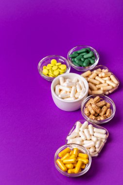 Organik beslenme takviyeleri, yukarıdan menekşe arkaplan üzerinde küçük kaselerde birçok vitamin ve mineral kapsülü. Besin takviyeleri, haplar ve tabletler, üst görünüm. Sağlıklı yaşam tarzı.