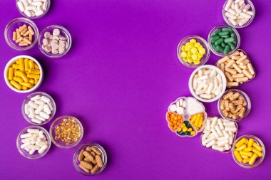 Organik beslenme takviyeleri, yukarıdan menekşe arkaplan üzerinde küçük kaselerde birçok vitamin ve mineral kapsülü. Besin takviyeleri, haplar ve tabletler, üst görünüm. Sağlıklı yaşam tarzı.