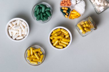 Organik beslenme takviyeleri, yukarıdan gri arka planda küçük kaselerde birçok vitamin ve mineral kapsülü. Besin takviyeleri, haplar ve tabletler, üst görünüm. Sağlıklı yaşam tarzı.