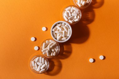 Organik beslenme takviyeleri, yukarıdan turuncu arka planda küçük kaselerde birçok vitamin ve mineral kapsülü. Besin takviyeleri, haplar ve tabletler, üst görünüm. Sağlıklı yaşam tarzı.