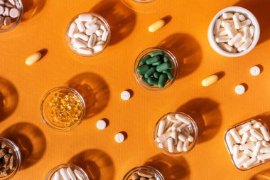 Organik beslenme takviyeleri, yukarıdan turuncu arka planda küçük kaselerde birçok vitamin ve mineral kapsülü. Besin takviyeleri, haplar ve tabletler, üst görünüm. Sağlıklı yaşam tarzı.