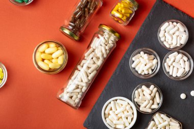 A, B, C, D vitamini ve turuncu arka plandaki cam kavanozlar gibi birçok farklı besin takviyesi hapı, mineral ve vitamin. Vitaminler ve sağlığın gelişmesi için.