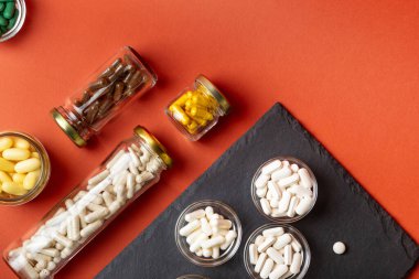 A, B, C, D vitamini ve turuncu arka plandaki cam kavanozlar gibi birçok farklı besin takviyesi hapı, mineral ve vitamin. Vitaminler ve sağlığın gelişmesi için.