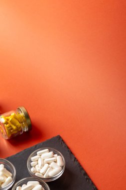 A, B, C, D vitamini ve turuncu arka plandaki cam kavanozlar gibi birçok farklı besin takviyesi hapı, mineral ve vitamin. Vitaminler ve sağlığın gelişmesi için.