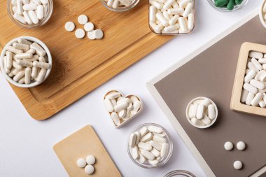 Different dietary supplement pills, minerals and vitamins such as such as vitamin d3, a, e, b, c, magnesium, zinc and calcium in beautiful composition from above on a wooden desk on white background. clipart