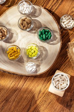 D3, a, b, c, e, k, magnezyum, çinko ve multivitamin hapları gibi organik gıda takviyeleri, vitamin ve mineraller yukarıdan küçük tabaklar halinde ahşap masa üzerinde güneş ışığı altında