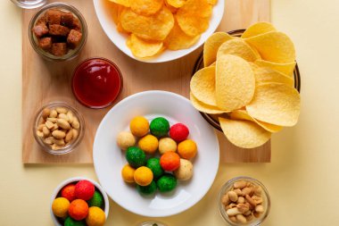 Farklı atıştırmalıklar, mesela cips, kraker, tuzlu fındık, bej arka plandaki ahşap masada wasabi fındığı..