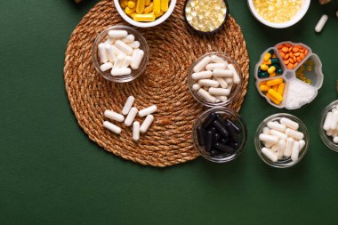 Birçok renkli vitamin ve mineral, beslenme takviyeleri, bağışıklık sistemini geliştirmek ve insan sağlığını desteklemek için çeşitli haplar ve tabletler. Yukarıdan gelen vitaminler ve besin takviyeleri koyu yeşil arka planda. Kırsal stil, üst görünüm. Sağlıklı yaşam.
