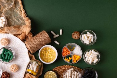 Birçok renkli vitamin ve mineral, beslenme takviyeleri, bağışıklık sistemini geliştirmek ve insan sağlığını desteklemek için çeşitli haplar ve tabletler. Yukarıdan gelen vitaminler ve besin takviyeleri koyu yeşil arka planda. Kırsal stil, üst görünüm. Sağlıklı yaşam.