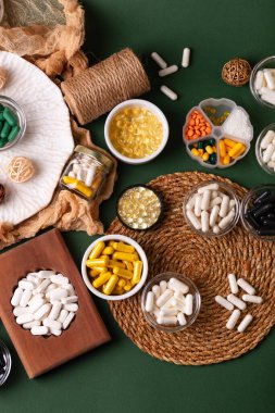 Birçok renkli vitamin ve mineral, beslenme takviyeleri, bağışıklık sistemini geliştirmek ve insan sağlığını desteklemek için çeşitli haplar ve tabletler. Yukarıdan gelen vitaminler ve besin takviyeleri koyu yeşil arka planda. Kırsal stil, üst görünüm. Sağlıklı yaşam.