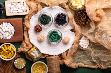 Birçok renkli vitamin ve mineral, beslenme takviyeleri, bağışıklık sistemini geliştirmek ve insan sağlığını desteklemek için çeşitli haplar ve tabletler. Yukarıdan gelen vitaminler ve besin takviyeleri koyu yeşil arka planda. Kırsal stil, üst görünüm. Sağlıklı yaşam.