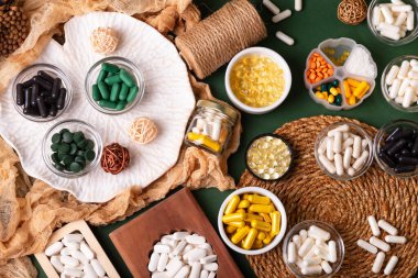 Birçok renkli vitamin ve mineral, beslenme takviyeleri, bağışıklık sistemini geliştirmek ve insan sağlığını desteklemek için çeşitli haplar ve tabletler. Yukarıdan gelen vitaminler ve besin takviyeleri koyu yeşil arka planda. Kırsal stil, üst görünüm. Sağlıklı yaşam.