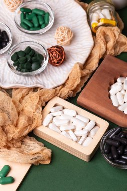 Birçok renkli vitamin ve mineral, beslenme takviyeleri, bağışıklık sistemini geliştirmek ve insan sağlığını desteklemek için çeşitli haplar ve tabletler. Yukarıdan gelen vitaminler ve besin takviyeleri koyu yeşil arka planda. Kırsal stil, üst görünüm. Sağlıklı yaşam.