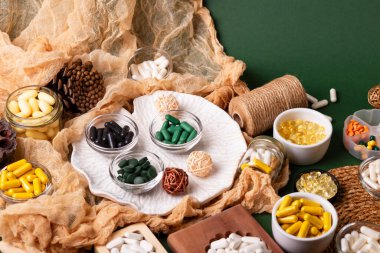Birçok renkli vitamin ve mineral, beslenme takviyeleri, bağışıklık sistemini geliştirmek ve insan sağlığını desteklemek için çeşitli haplar ve tabletler. Yukarıdan gelen vitaminler ve besin takviyeleri koyu yeşil arka planda. Kırsal stil, üst görünüm. Sağlıklı yaşam.