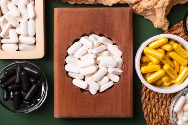 Birçok renkli vitamin ve mineral, beslenme takviyeleri, bağışıklık sistemini geliştirmek ve insan sağlığını desteklemek için çeşitli haplar ve tabletler. Koyu yeşil arka planda yukarıdaki kavanozlarda vitaminler.