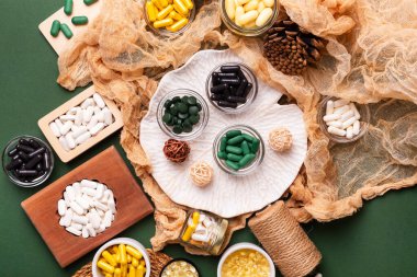 Birçok renkli vitamin ve mineral, beslenme takviyeleri, bağışıklık sistemini geliştirmek ve insan sağlığını desteklemek için çeşitli haplar ve tabletler. Yukarıdan gelen vitaminler ve besin takviyeleri koyu yeşil arka planda. Kırsal stil, üst görünüm. Sağlıklı yaşam.
