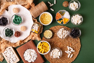 Birçok renkli vitamin ve mineral, beslenme takviyeleri, bağışıklık sistemini geliştirmek ve insan sağlığını desteklemek için çeşitli haplar ve tabletler. Yukarıdan gelen vitaminler ve besin takviyeleri koyu yeşil arka planda. Kırsal stil, üst görünüm. Sağlıklı yaşam.