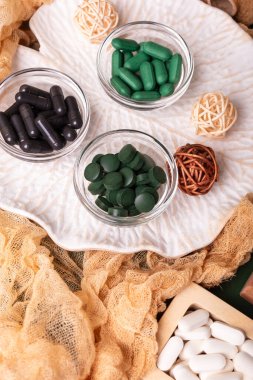 Birçok renkli vitamin ve mineral, beslenme takviyeleri, bağışıklık sistemini geliştirmek ve insan sağlığını desteklemek için çeşitli haplar ve tabletler. Yukarıdan gelen vitaminler ve besin takviyeleri koyu yeşil arka planda. Kırsal stil, üst görünüm. Sağlıklı yaşam.