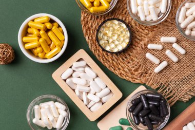 Birçok renkli vitamin ve mineral, beslenme takviyeleri, bağışıklık sistemini geliştirmek ve insan sağlığını desteklemek için çeşitli haplar ve tabletler. Yukarıdan gelen vitaminler ve besin takviyeleri koyu yeşil arka planda. Kırsal stil, üst görünüm. Sağlıklı yaşam.