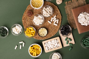 Birçok renkli vitamin ve mineral, beslenme takviyeleri, bağışıklık sistemini geliştirmek ve insan sağlığını desteklemek için çeşitli haplar ve tabletler. Yukarıdan gelen vitaminler ve besin takviyeleri koyu yeşil arka planda. Kırsal stil, üst görünüm. Sağlıklı yaşam.