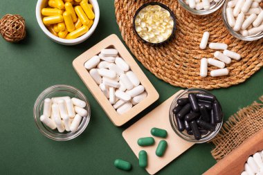 Birçok renkli vitamin ve mineral, beslenme takviyeleri, bağışıklık sistemini geliştirmek ve insan sağlığını desteklemek için çeşitli haplar ve tabletler. Yukarıdan gelen vitaminler ve besin takviyeleri koyu yeşil arka planda. Kırsal stil, üst görünüm. Sağlıklı yaşam.