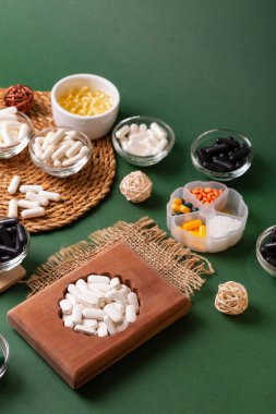 Birçok renkli vitamin ve mineral, beslenme takviyeleri, bağışıklık sistemini geliştirmek ve insan sağlığını desteklemek için çeşitli haplar ve tabletler. Yukarıdan gelen vitaminler ve besin takviyeleri koyu yeşil arka planda. Kırsal stil, üst görünüm. Sağlıklı yaşam.
