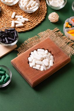 Birçok renkli vitamin ve mineral, beslenme takviyeleri, bağışıklık sistemini geliştirmek ve insan sağlığını desteklemek için çeşitli haplar ve tabletler. Yukarıdan gelen vitaminler ve besin takviyeleri koyu yeşil arka planda. Kırsal stil, üst görünüm. Sağlıklı yaşam.