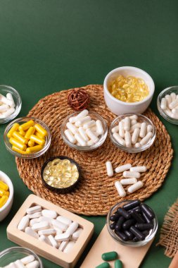 Birçok renkli vitamin ve mineral, beslenme takviyeleri, bağışıklık sistemini geliştirmek ve insan sağlığını desteklemek için çeşitli haplar ve tabletler. Yukarıdan gelen vitaminler ve besin takviyeleri koyu yeşil arka planda. Kırsal stil, üst görünüm. Sağlıklı yaşam.