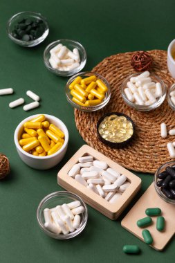 Birçok renkli vitamin ve mineral, beslenme takviyeleri, bağışıklık sistemini geliştirmek ve insan sağlığını desteklemek için çeşitli haplar ve tabletler. Yukarıdan gelen vitaminler ve besin takviyeleri koyu yeşil arka planda. Kırsal stil, üst görünüm. Sağlıklı yaşam.