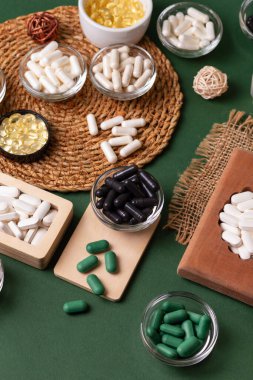 Birçok renkli vitamin ve mineral, beslenme takviyeleri, bağışıklık sistemini geliştirmek ve insan sağlığını desteklemek için çeşitli haplar ve tabletler. Yukarıdan gelen vitaminler ve besin takviyeleri koyu yeşil arka planda. Kırsal stil, üst görünüm. Sağlıklı yaşam.