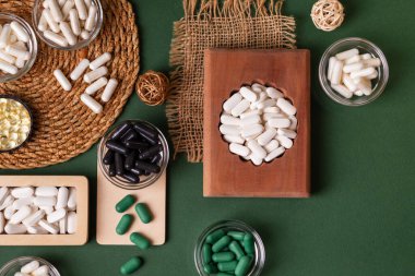 Birçok renkli vitamin ve mineral, beslenme takviyeleri, bağışıklık sistemini geliştirmek ve insan sağlığını desteklemek için çeşitli haplar ve tabletler. Yukarıdan gelen vitaminler ve besin takviyeleri koyu yeşil arka planda. Kırsal stil, üst görünüm. Sağlıklı yaşam.