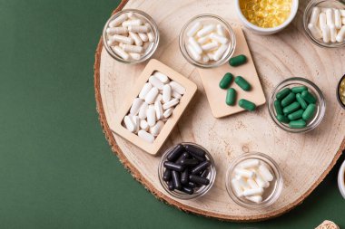 Birçok renkli vitamin ve mineral, beslenme takviyeleri, bağışıklık sistemini geliştirmek ve insan sağlığını desteklemek için çeşitli haplar ve tabletler. Koyu yeşil arka planda yukarıdaki kavanozlarda vitaminler.