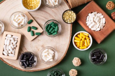 Birçok renkli vitamin ve mineral, beslenme takviyeleri, bağışıklık sistemini geliştirmek ve insan sağlığını desteklemek için çeşitli haplar ve tabletler. Koyu yeşil arka planda yukarıdaki kavanozlarda vitaminler.
