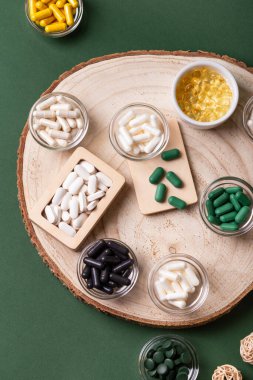 Birçok renkli vitamin ve mineral, beslenme takviyeleri, bağışıklık sistemini geliştirmek ve insan sağlığını desteklemek için çeşitli haplar ve tabletler. Koyu yeşil arka planda yukarıdaki kavanozlarda vitaminler.