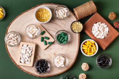 Birçok renkli vitamin ve mineral, beslenme takviyeleri, bağışıklık sistemini geliştirmek ve insan sağlığını desteklemek için çeşitli haplar ve tabletler. Koyu yeşil arka planda yukarıdaki kavanozlarda vitaminler.