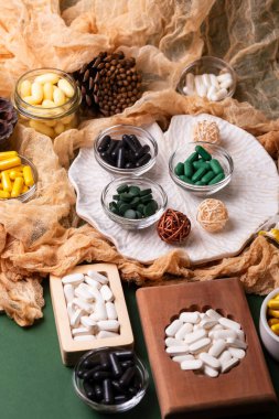 Birçok renkli vitamin ve mineral, beslenme takviyeleri, bağışıklık sistemini geliştirmek ve insan sağlığını desteklemek için çeşitli haplar ve tabletler. Yukarıdan gelen vitaminler ve besin takviyeleri koyu yeşil arka planda. Kırsal stil, üst görünüm. Sağlıklı yaşam.