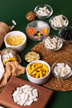 Birçok renkli vitamin ve mineral, beslenme takviyeleri, bağışıklık sistemini geliştirmek ve insan sağlığını desteklemek için çeşitli haplar ve tabletler. Yukarıdan gelen vitaminler ve besin takviyeleri koyu yeşil arka planda. Kırsal stil, üst görünüm. Sağlıklı yaşam.