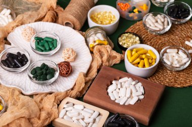 Birçok renkli vitamin ve mineral, beslenme takviyeleri, bağışıklık sistemini geliştirmek ve insan sağlığını desteklemek için çeşitli haplar ve tabletler. Yukarıdan gelen vitaminler ve besin takviyeleri koyu yeşil arka planda. Kırsal stil, üst görünüm. Sağlıklı yaşam.